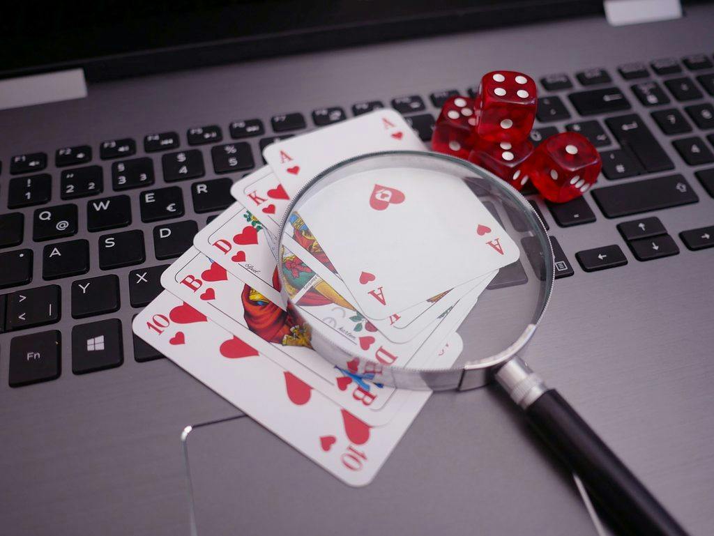 Lupa sobre un as de corazones y otras cartas de póker, con dos dados rojos, encima del teclado de un portátil